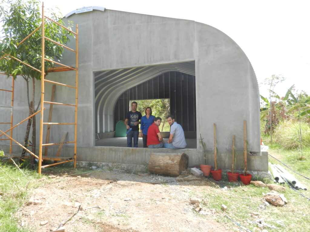 Una familia en la abertura de una estructura arqueada de acero (Modelo A de SteelMaster). La estructura tiene los arcos terminados y paredes de extremo terminadas también. Hay un andamio al lado de la estructura.