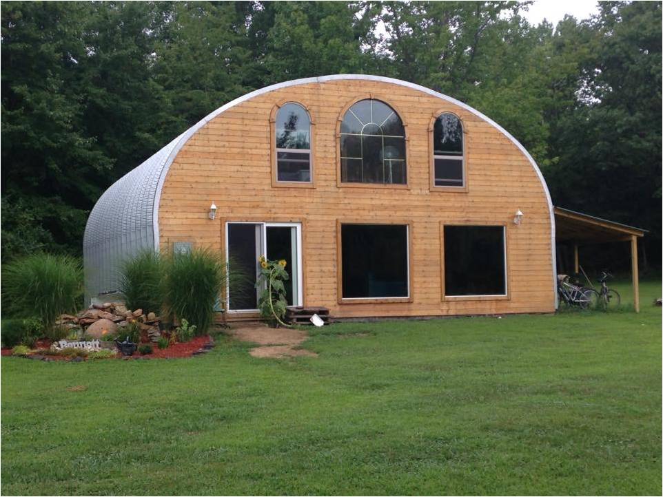 Una casa construida con el Modelo S de SteelMaster. Hay algunas ventanas y una puerta en la pared de extremo de madera. También hay un jardín y un porche con bicicletas.