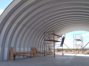 Una vista interior de la construcción de una estructura arqueada de acero. Hay andamios y un trabajador.