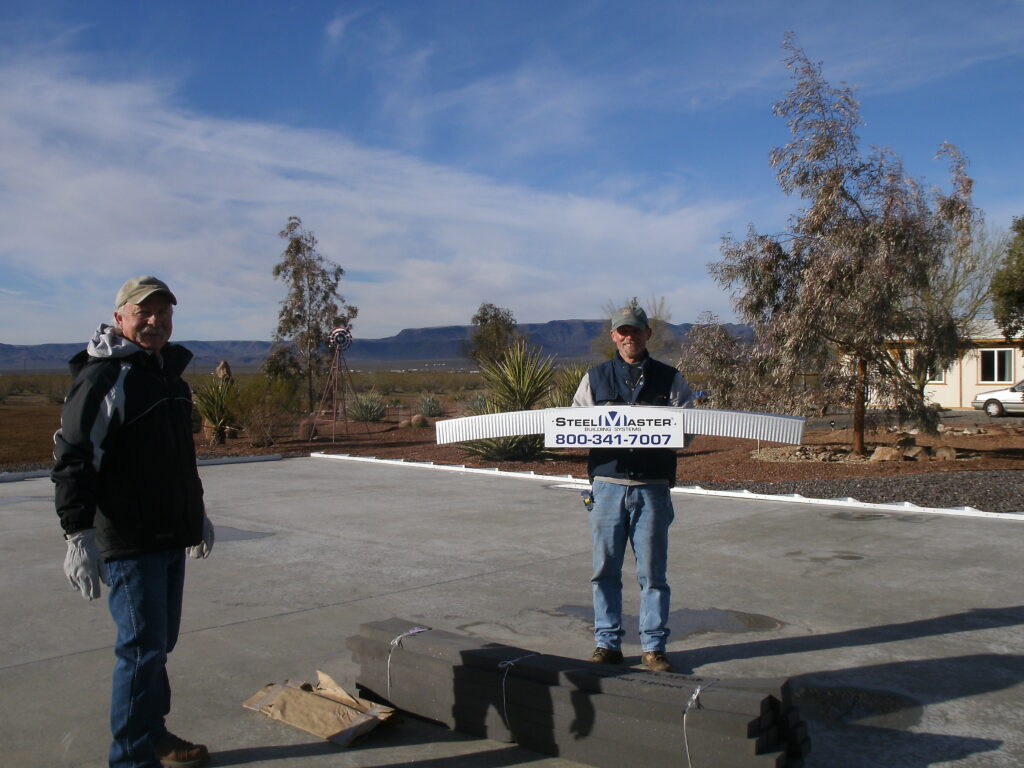 Dos personas sobre una cimentación de concreto. Uno está sosteniendo una pieza de acero de una estructura SteelMaster.