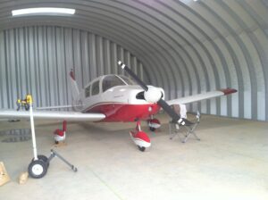 Una vista interior de un hangar para aeronave. Es un modelo S de SteelMaster--una estructura arqueada de acero. El avión es pequeño y blanco.