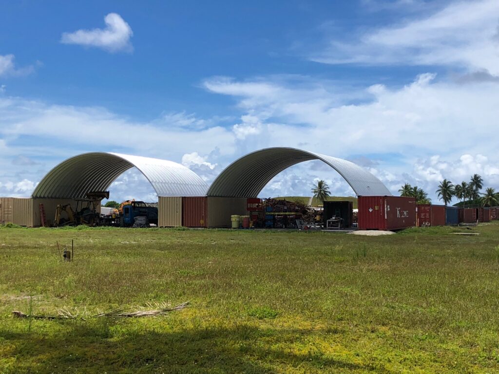 Dos cubiertas de contenedores una al lado de la otra. Los techos son arcos de acero. Debajo de las cubiertas hay vehículos de construcción.