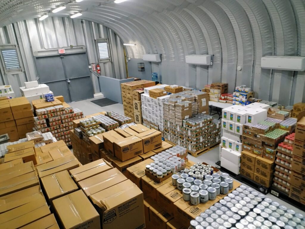 Una vista interior de un banco de alimentos. Hay latas de comida y muchas cajas.